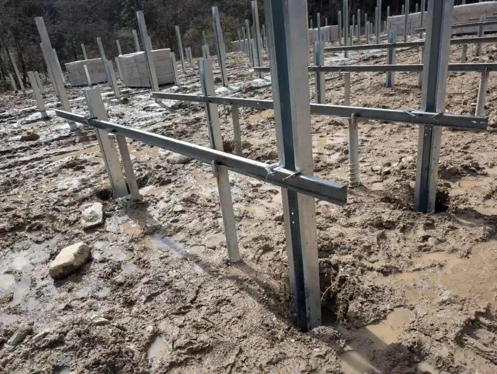 Close-up of SR Solar galvanized steel C-steel beams and connectors on a muddy terrain