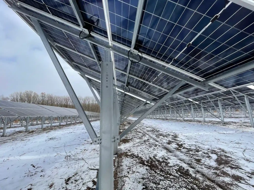 An under-array view of SR Solar ground mounting solutions showcasing robust steel post and rail engineering beneath solar panels on a snowy site.