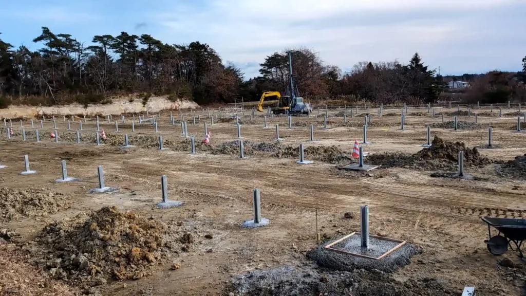 Construction site of SR Solar ground mounting systems showing concrete foundations and vertical pillars for the ACT DREAM solar project in Fukushima Soma.