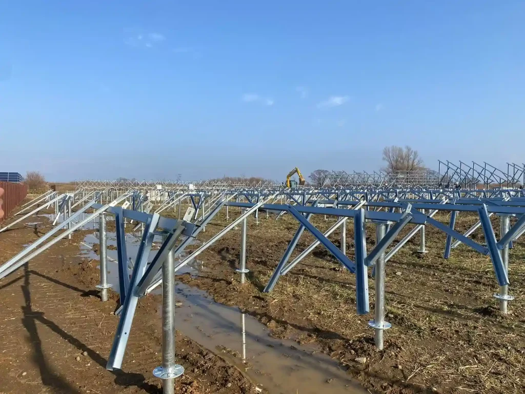 Initial triangular mounting legs installed on ground screws by SR Solar with an excavator working in the background.