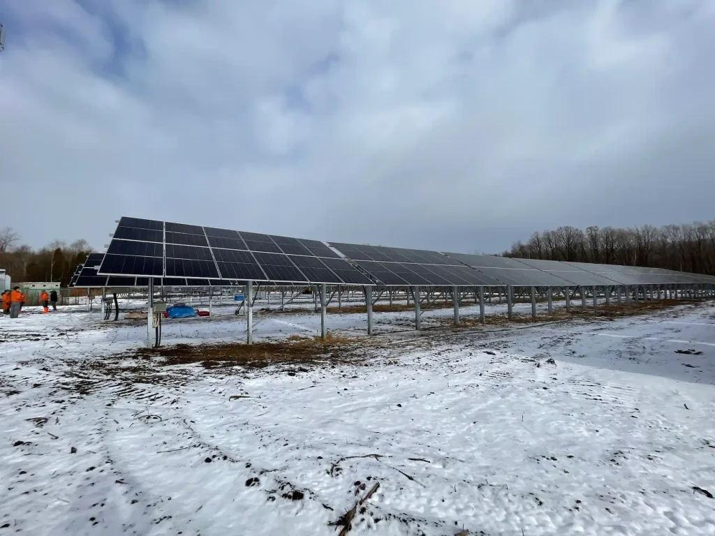 An extensive row of SR Solar heavy snow ground-mounted solar panel arrays stretching across a snow-covered utility site under a cloudy sky.