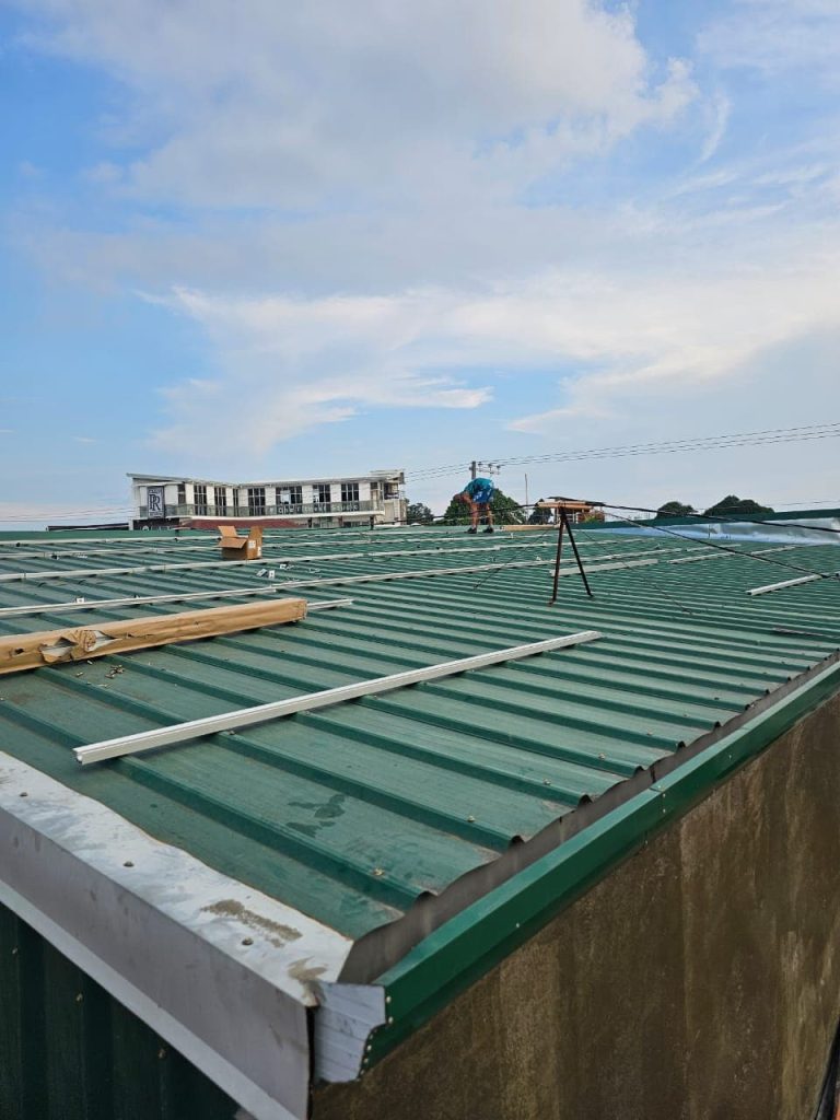 An installer positioning aluminum tracking rails for an SR Solar L-feet mounting system on a green corrugated metal roof in the Philippines.