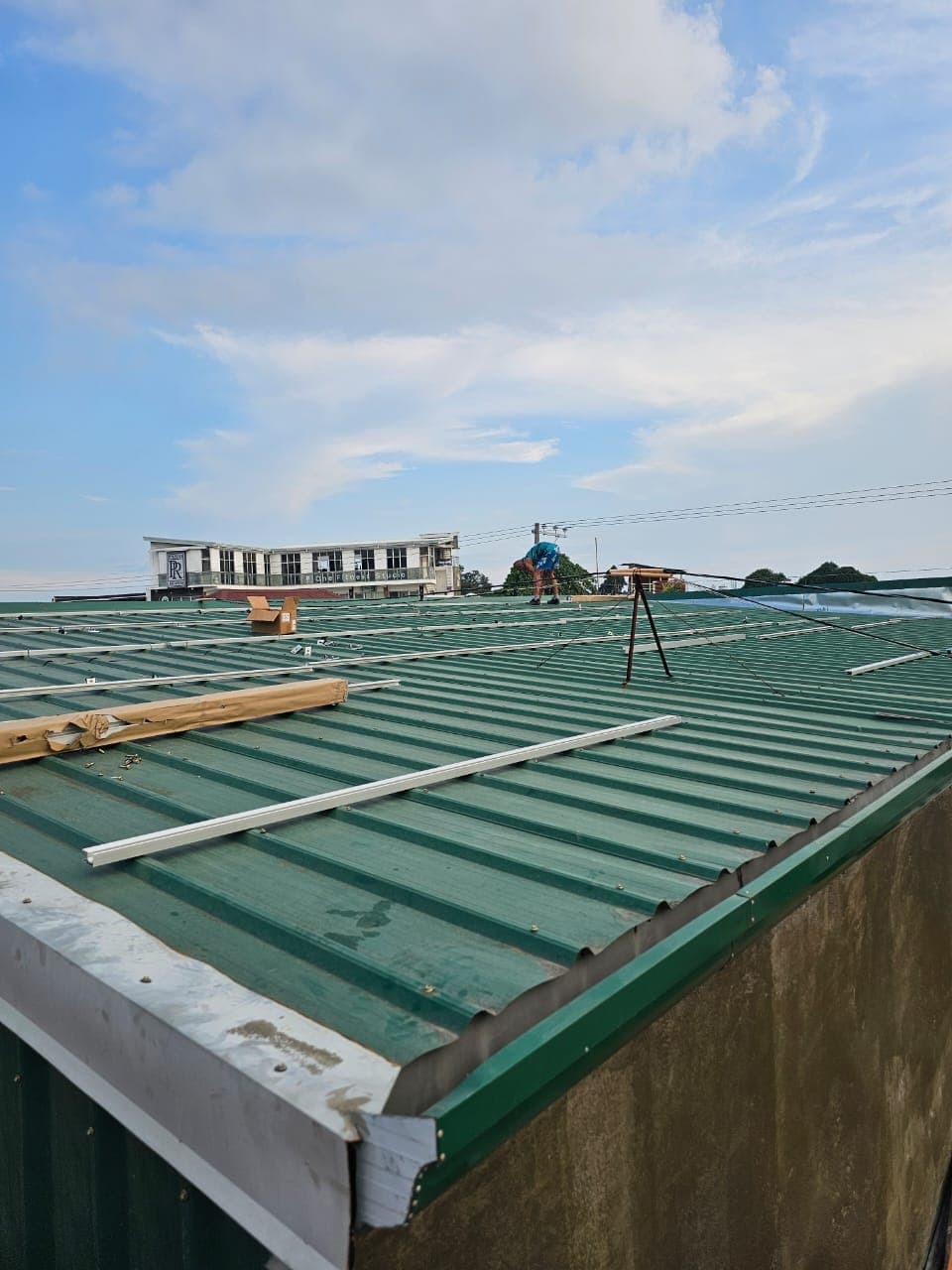 An installer positioning aluminum tracking rails for an SR Solar L-feet mounting system on a green corrugated metal roof in the Philippines.