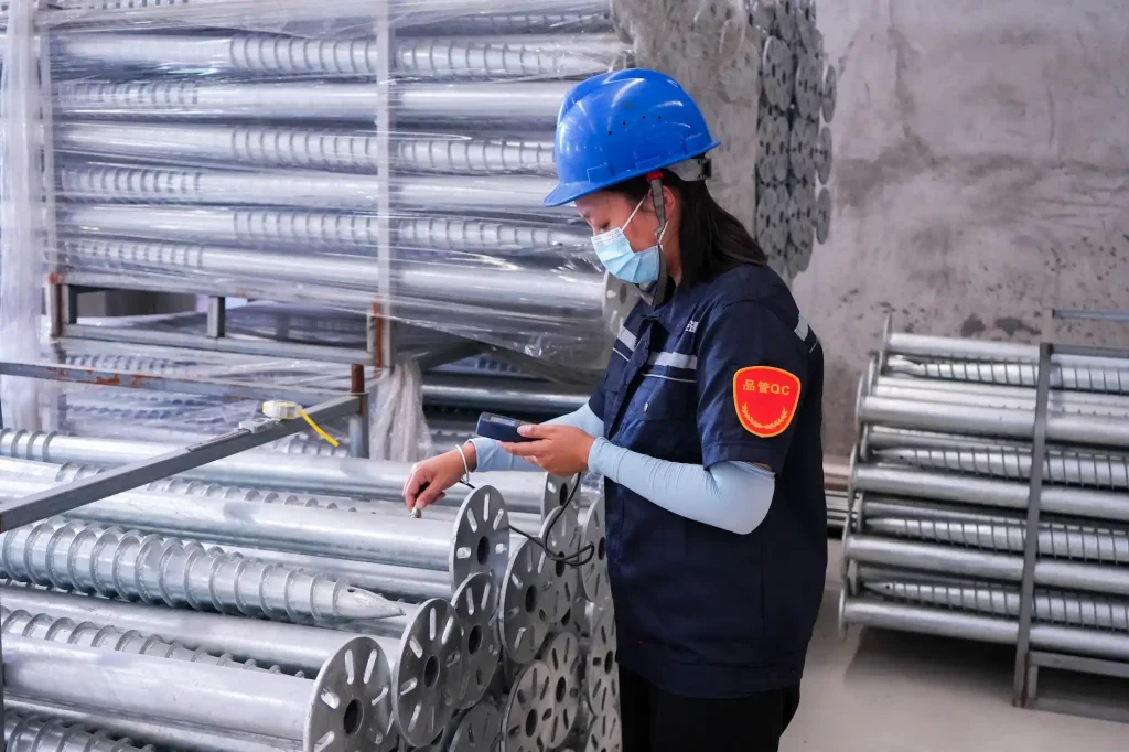 Quality assurance inspector verifying dimensions and thickness tolerances of ground screw pile hardware at the SR Solar factory.