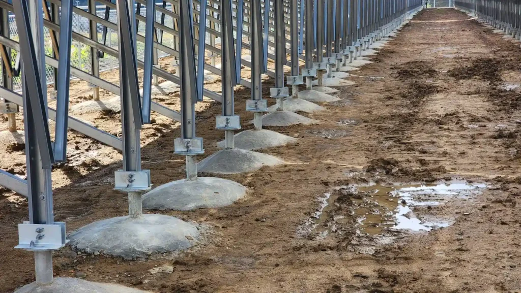 Side-angle close-up profile of a long row of concrete reinforced foundation pillars supporting SR Solar ZAM steel racking structures.