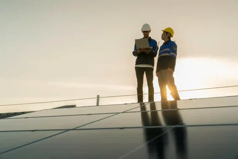 Two site engineers wearing safety hardhats and safety vests inspecting a solar roof mounting structure at dusk