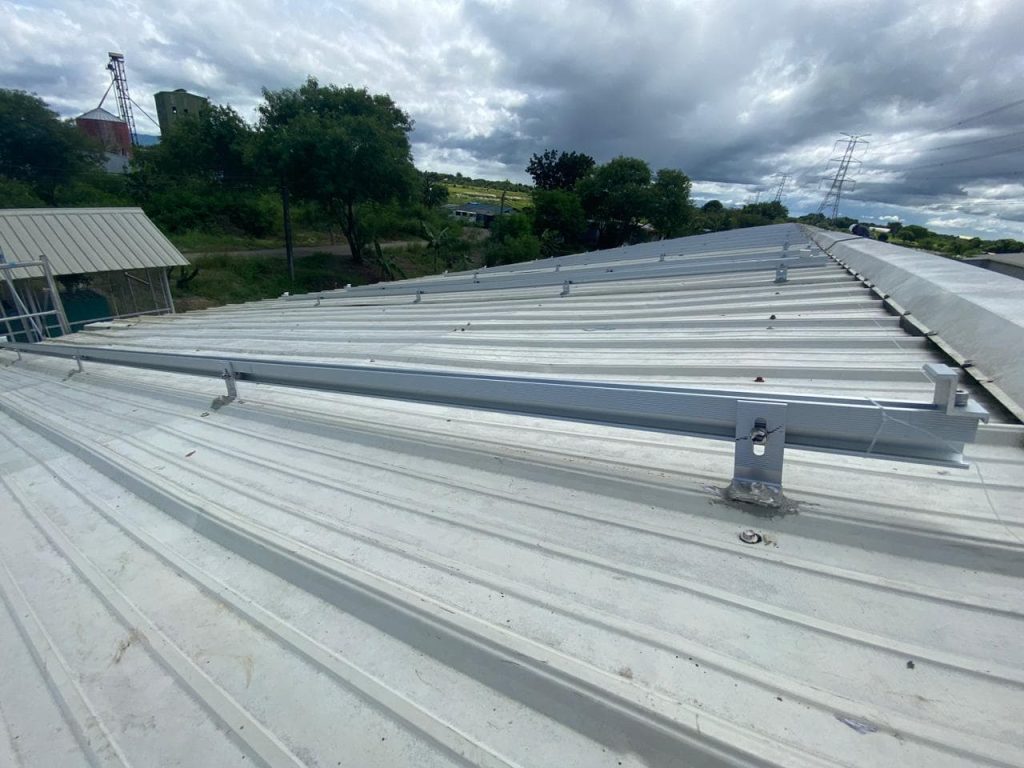 Close-up of SR Solar aluminum rails secured by heavy-duty L-feet brackets with waterproof EPDM rubber pads on a tin roof.