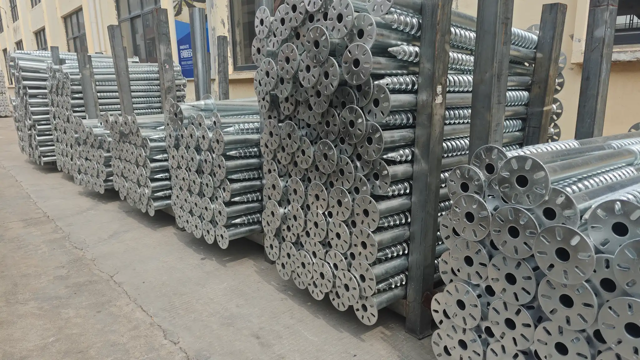 SR Solar flanged and continuous thread ground screw anchors neatly stacked in steel racks outdoors