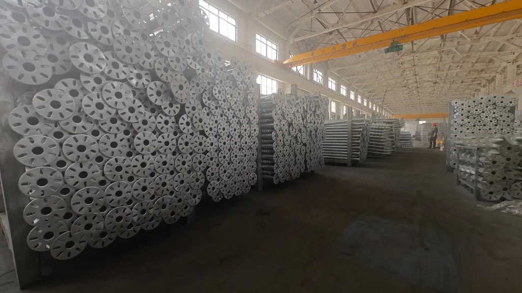SR Solar end-view stack of round flange plate ground screws inside large manufacturing workshop with overhead crane