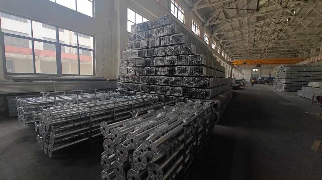SR Solar ground screw piles and stacked bundles of galvanized steel structural C-channels inside factory